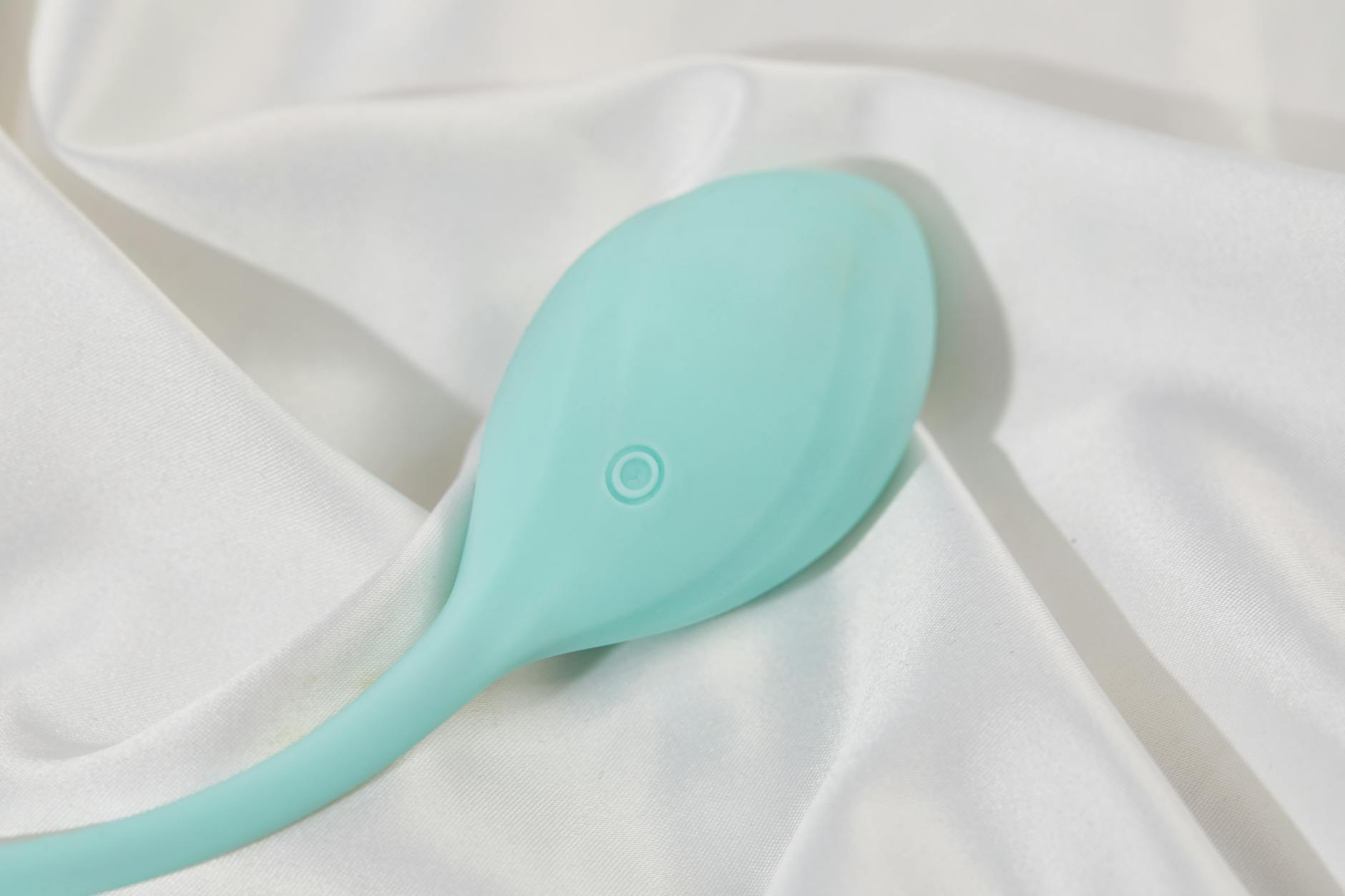 A teal lemon clitoral vibrator on white silk fabric, symbolizing reconnection and self-intimacy