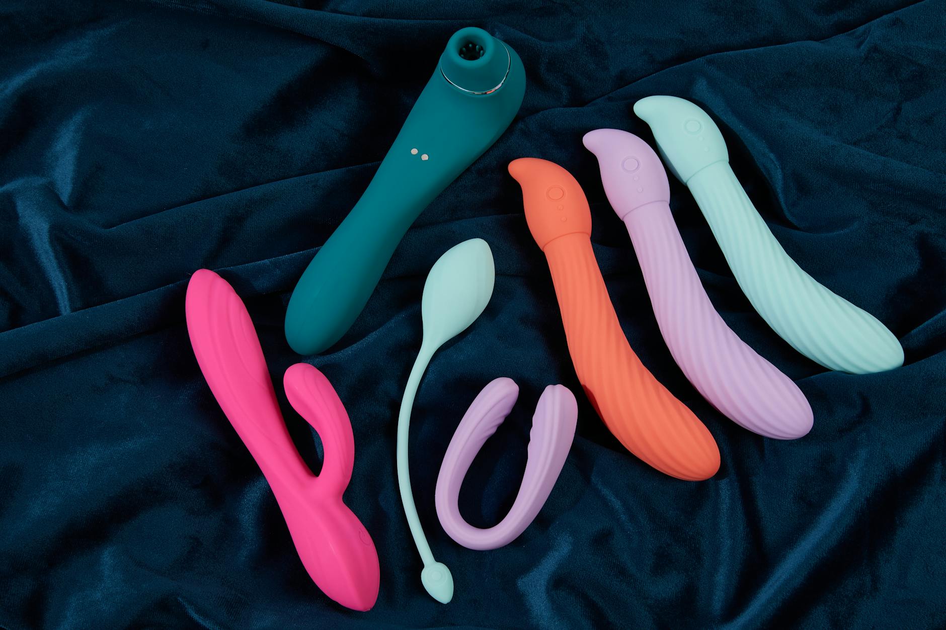 Collection of colorful silicone sex toys including clitoral vibrators displayed on dark blue fabric