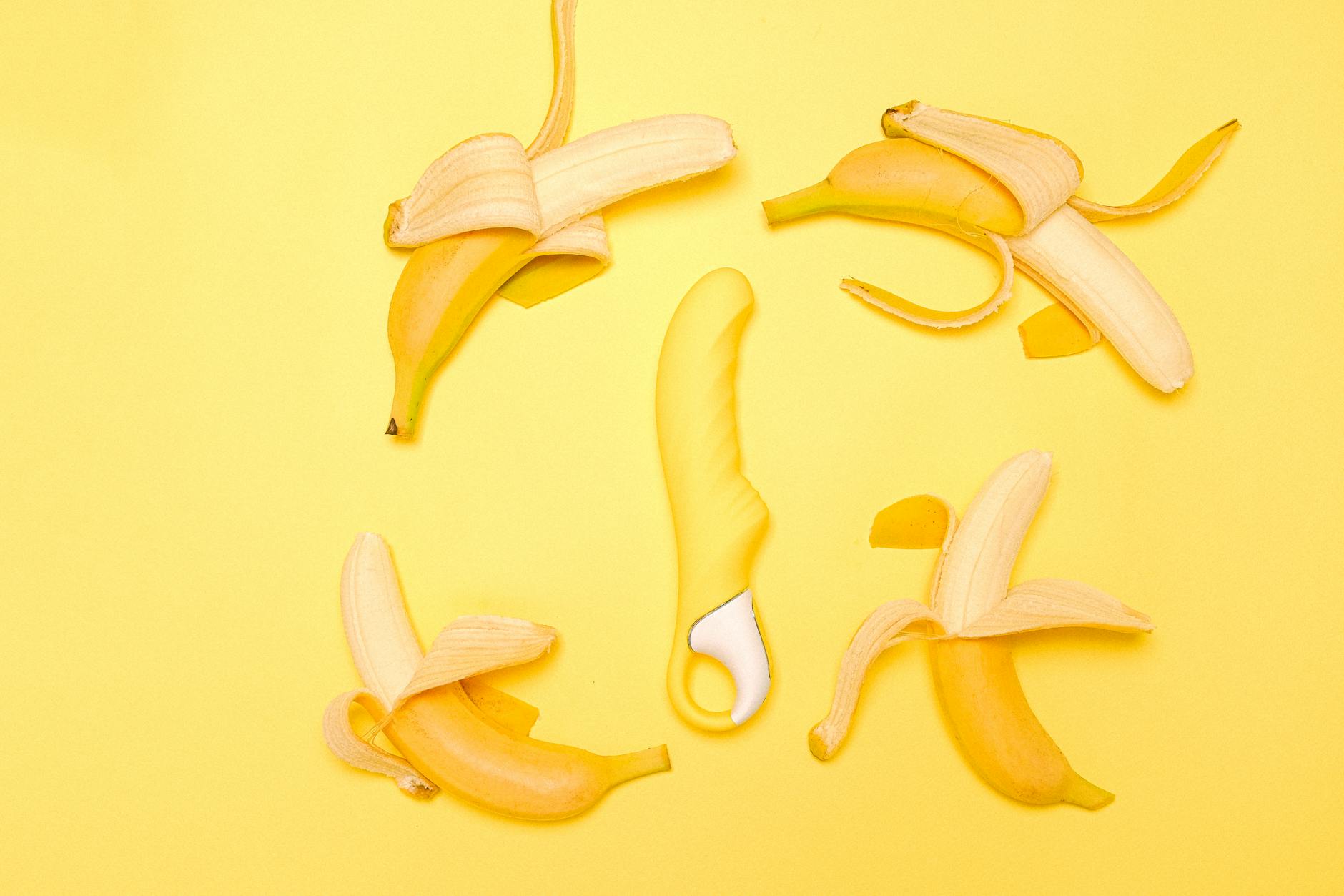 Yellow silicone vibrator surrounded by fresh lemons and peeled banana slices on a bright yellow background