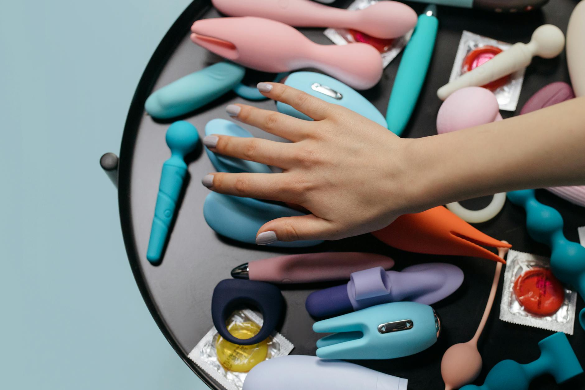 Woman with eyeglasses holding blue and pink silicone vibrators in a contemplative manner.