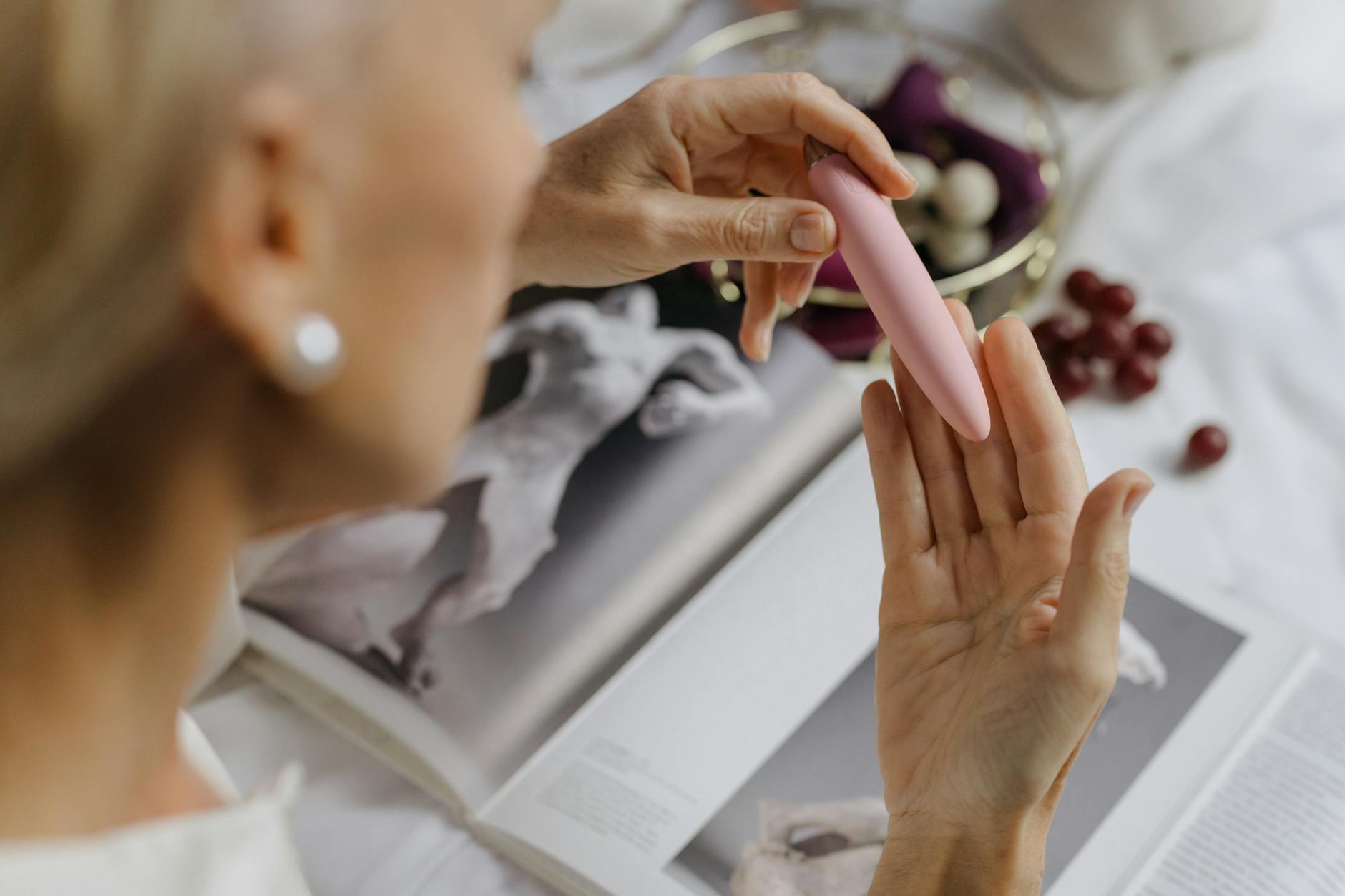 A woman holding a pink vibrator surrounded by personal wellness items, symbolizing self-discovery and intimate pleasure in midlife