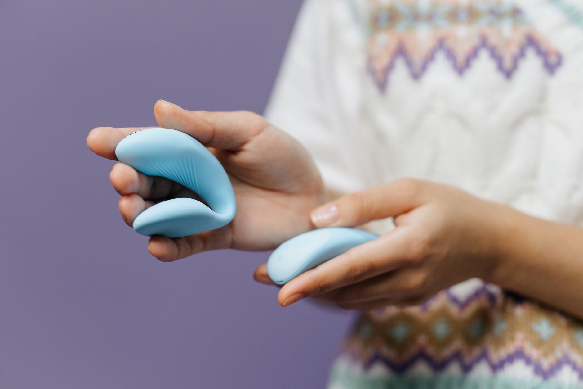 Close-up of hands holding a blue lemon vibrator against a purple background, symbolizing intimate connection and pleasure.